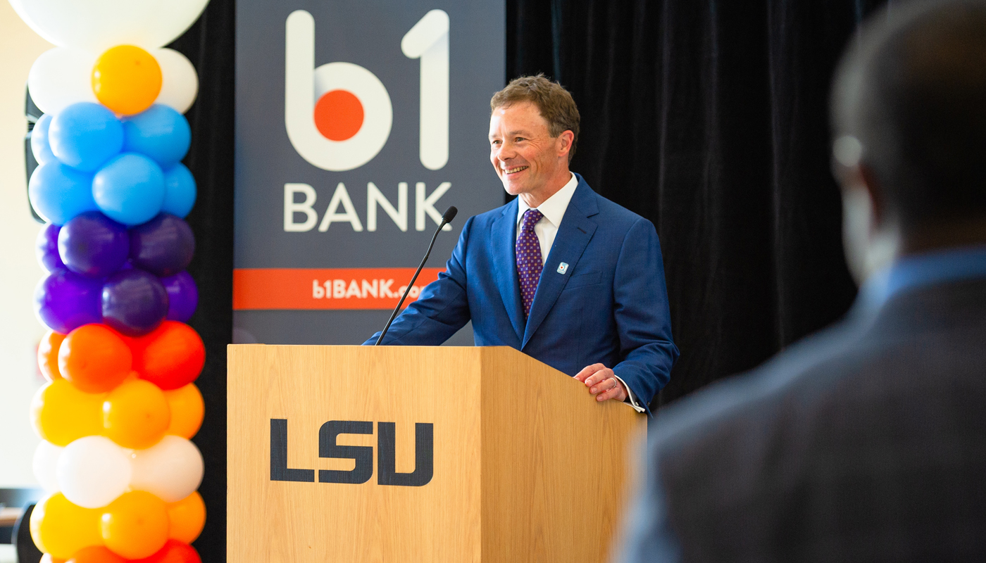 Man speaks at podium with B1BANK sign in background.