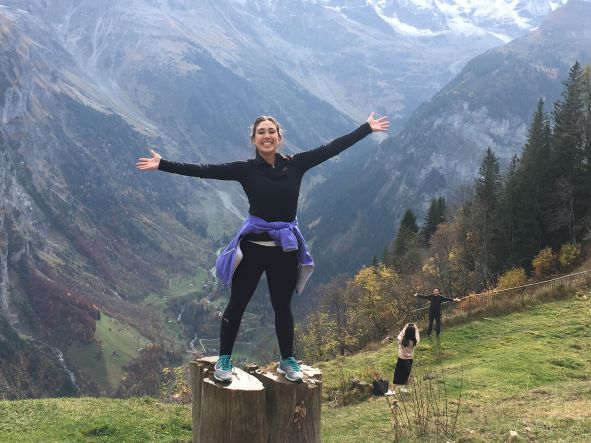 Single female student stands on rock in front of mountains