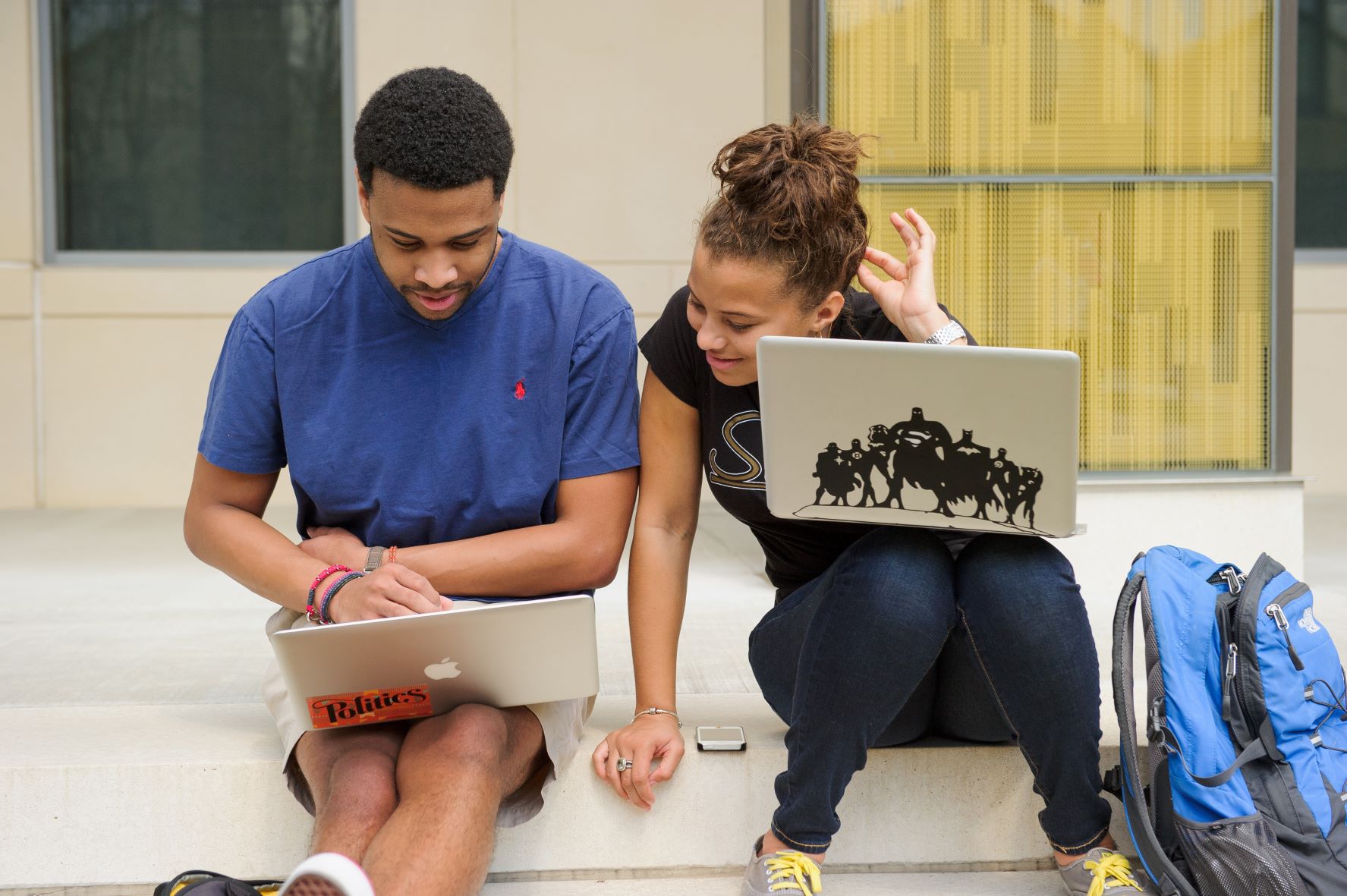 Two students sitting outside looks at laptops.