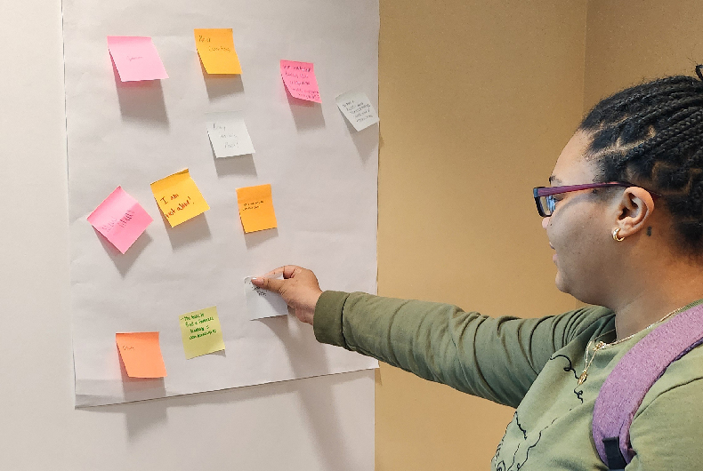 student putting a sticky note on a board during workshop