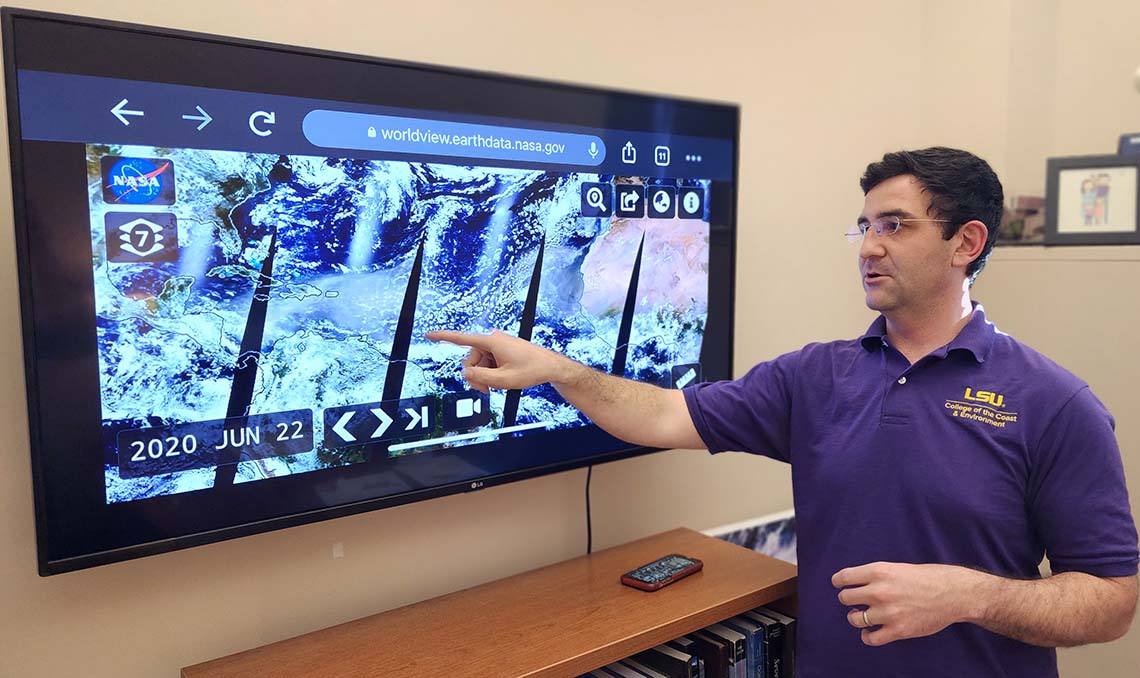 Paul Miller A man stands in front of a television with satellite imagery of the Earth on it