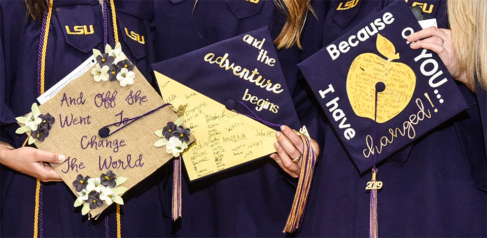 three graduates holding graduation caps with designs