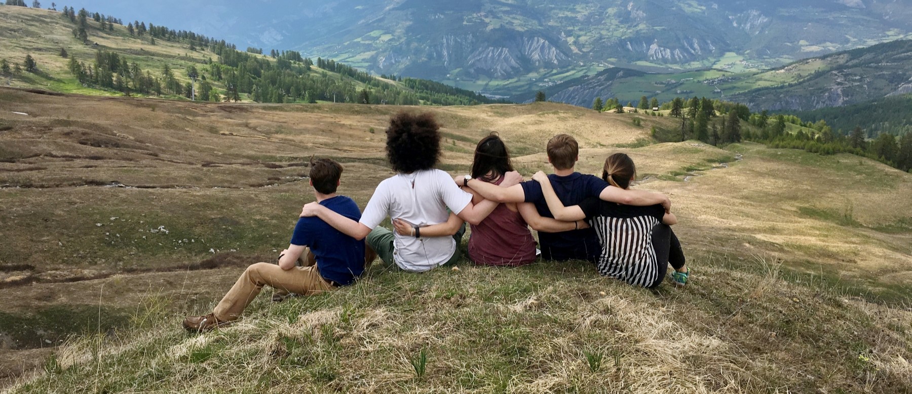 five students link arms and look out at a majestic mountain