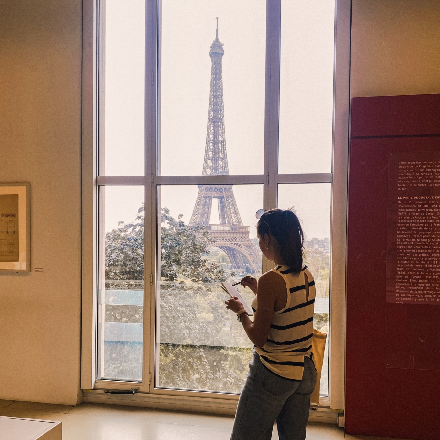 student sketches in sketchbook in front of Eiffel Tower