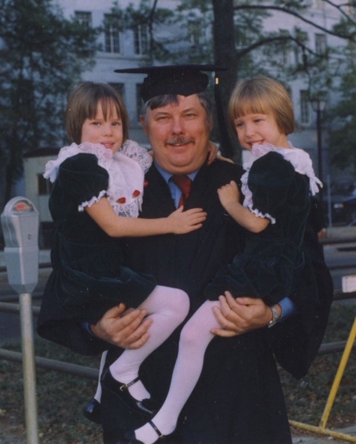 Hugghins at his graduation holding his twin daughters