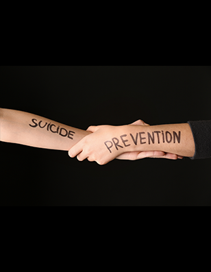 Photo of two arms grasping each other with the words suicide prevention in marker on the arms.