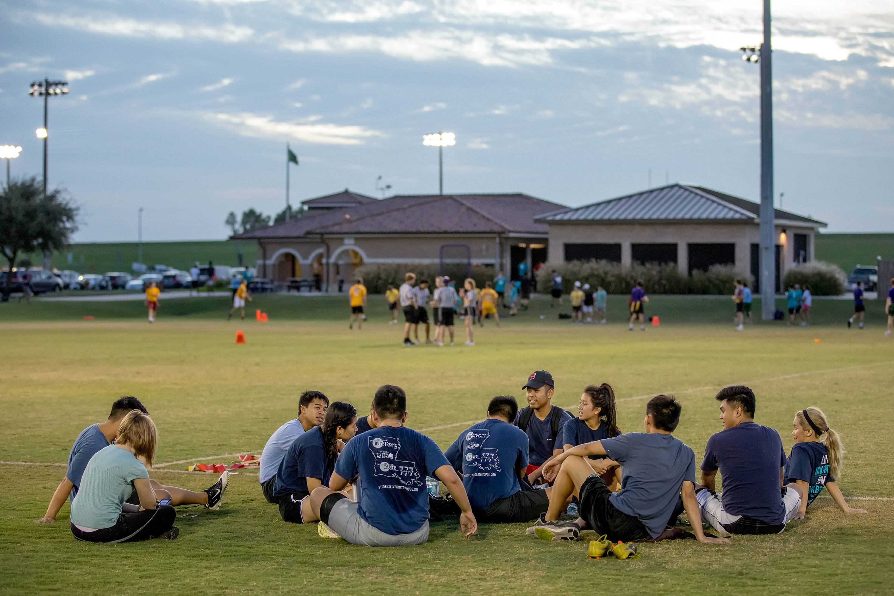 students sitting down in the grass of River Road Field Complex