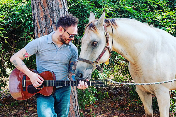 Charlie Rauh plays guitar for a horse